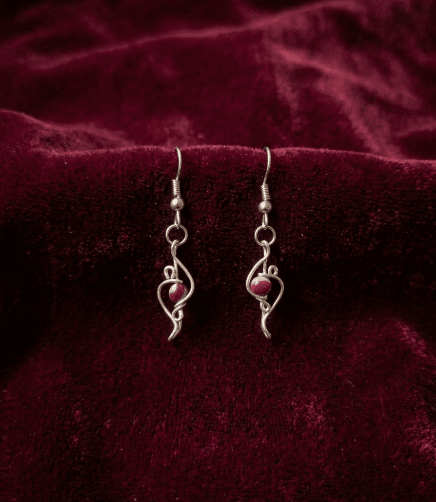 Loki’s Spark: Silver wire earrings with brown beads, showcased on red velvet fabric